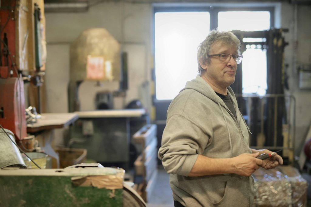 Side view of senior white hair worker in eyeglasses with cutter in hand working in workshop